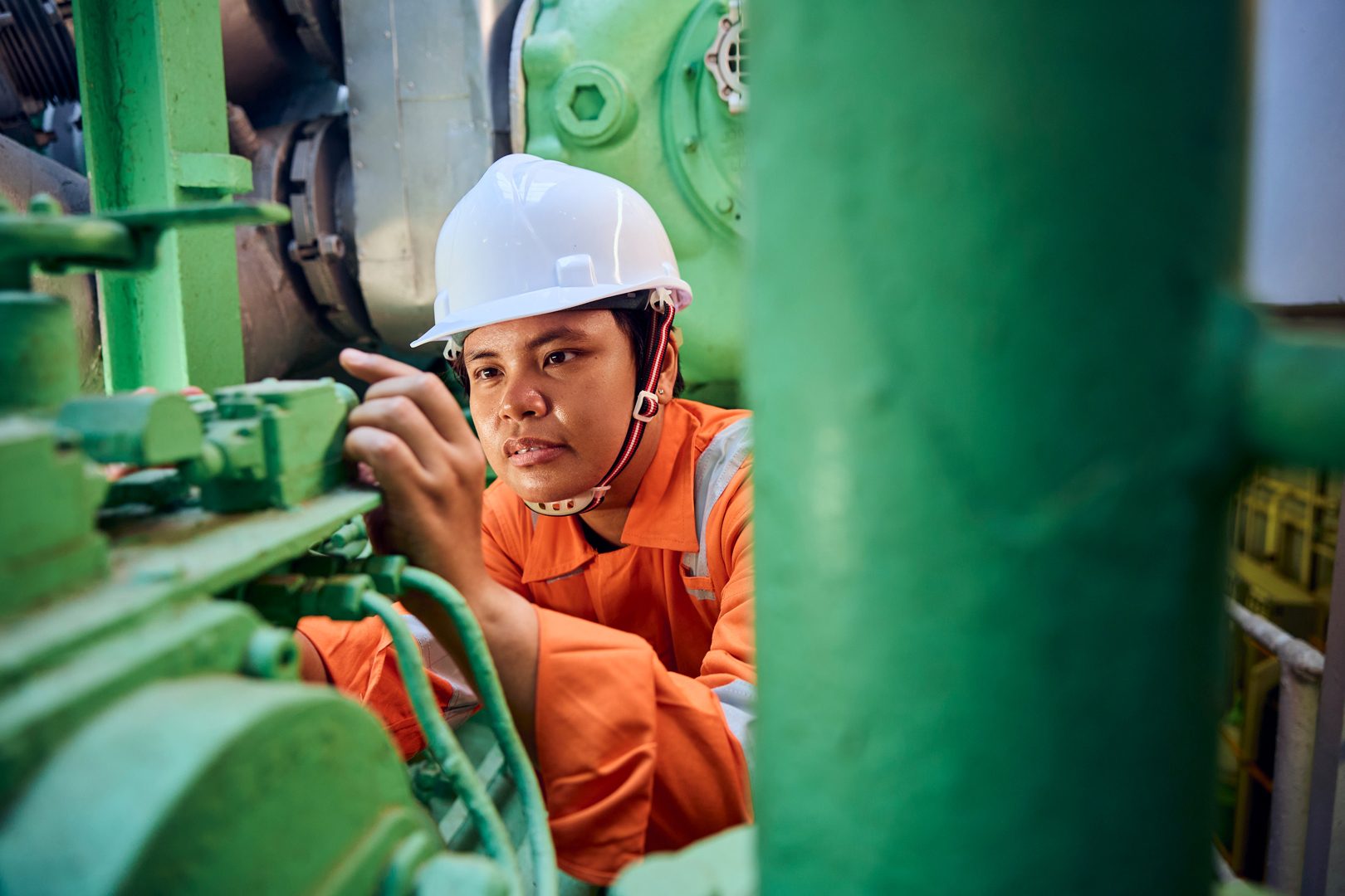 Worker in hard hat inspecting green machinery.