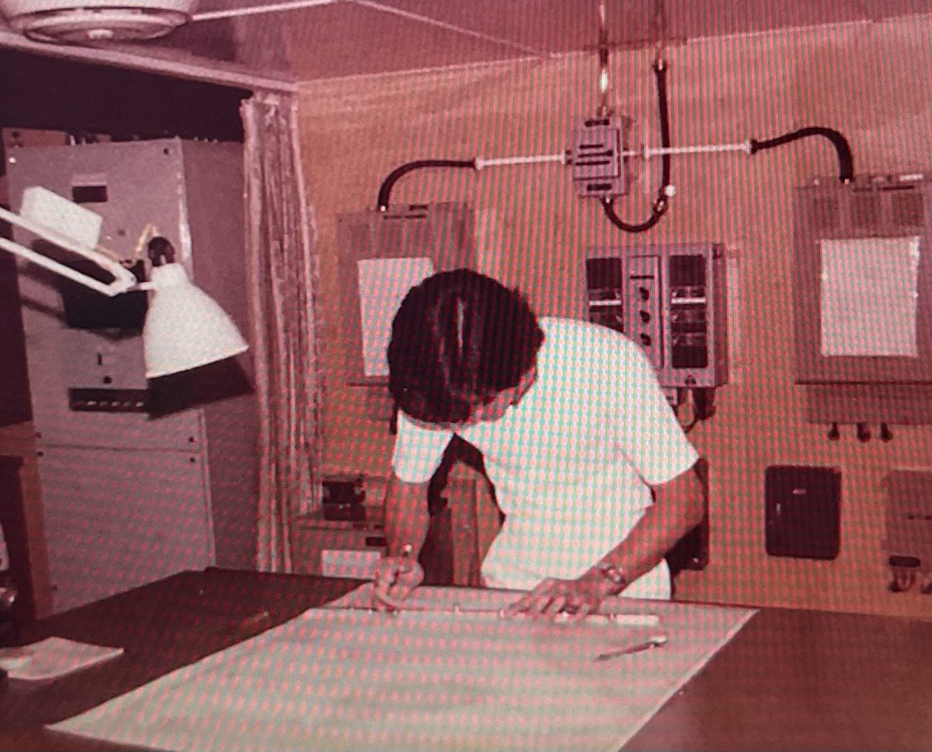 Person drafting blueprints at a large table, surrounded by industrial control panels.