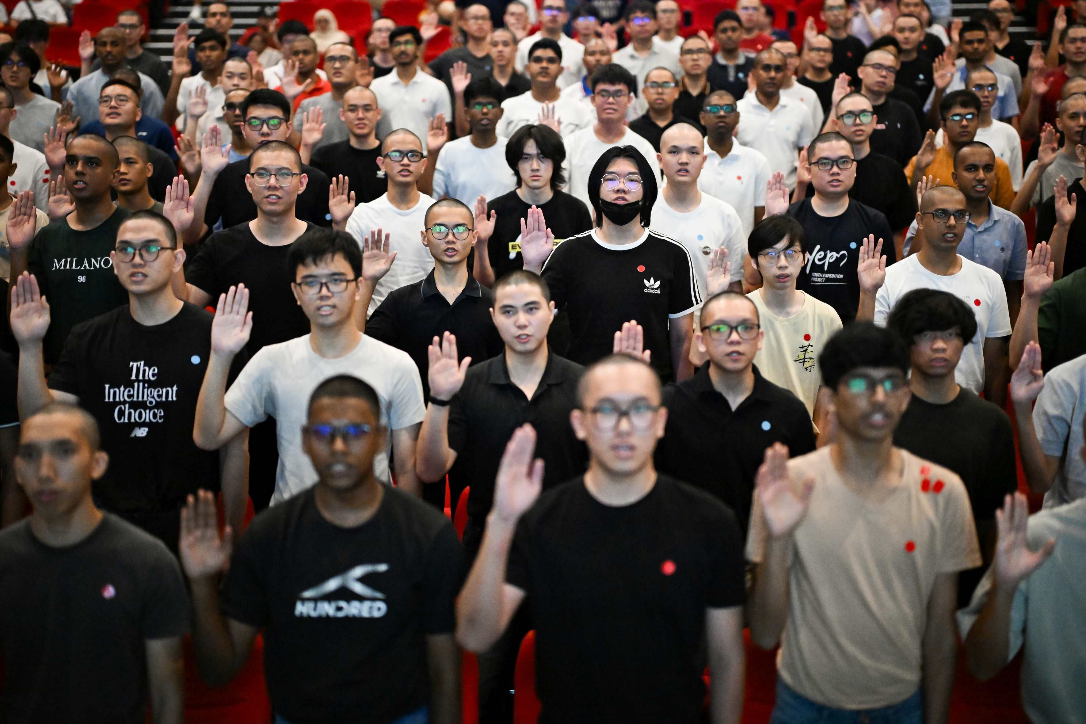People of various ages and races raise their arms and recite a pledge at the Basic Military Training Centre on Pulau Tekong.
