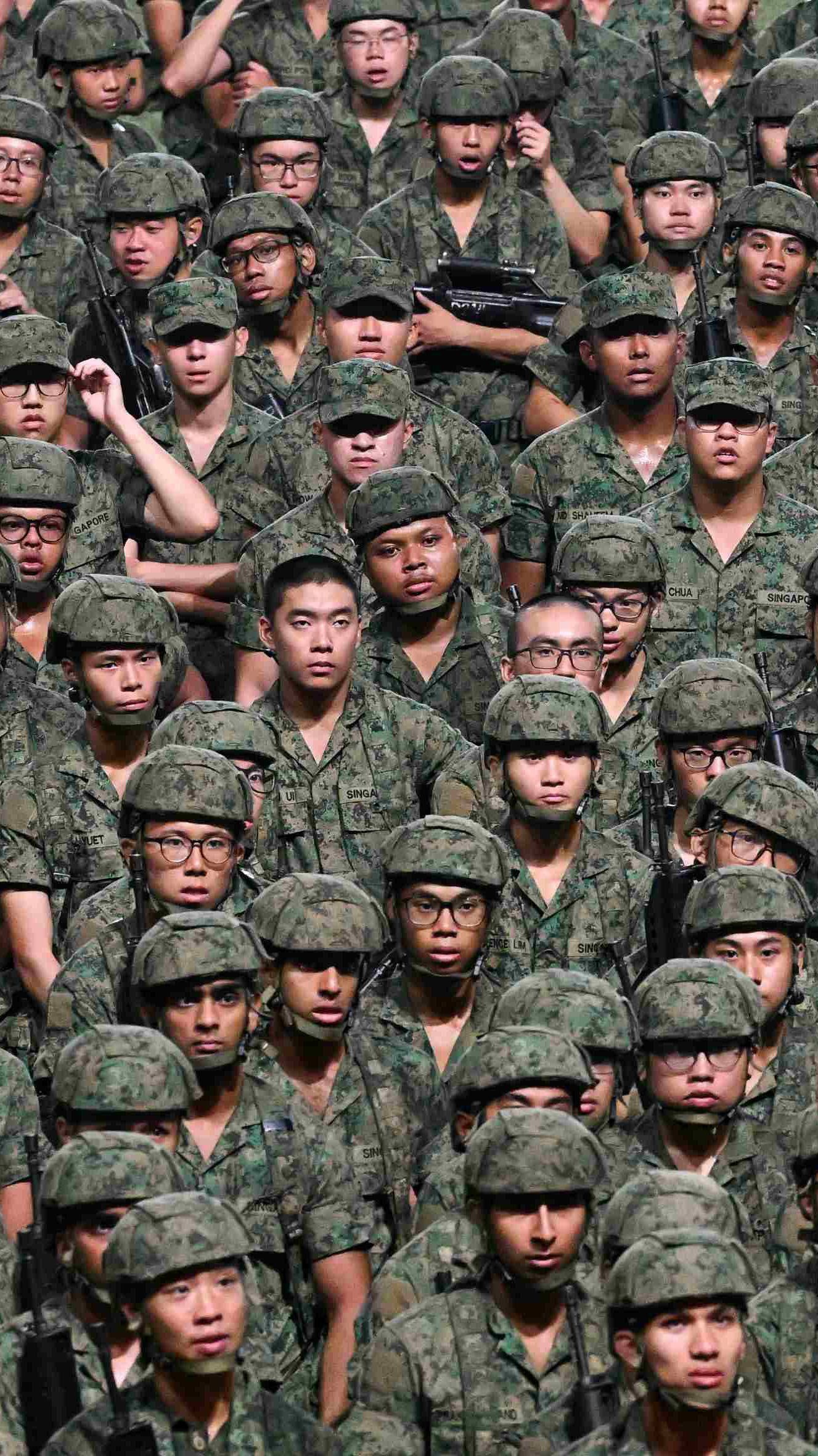 Group of people in singapore army uniform sitting in rows receiving instructions from a superior
